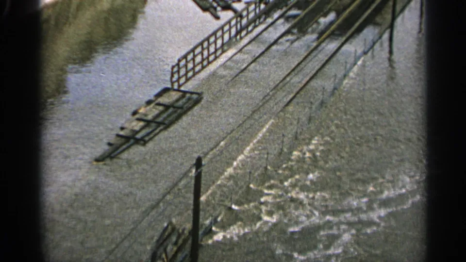 1965 Minnesota flood scene with moving water, metal railings, and industrial structures partly surrounded by high water.