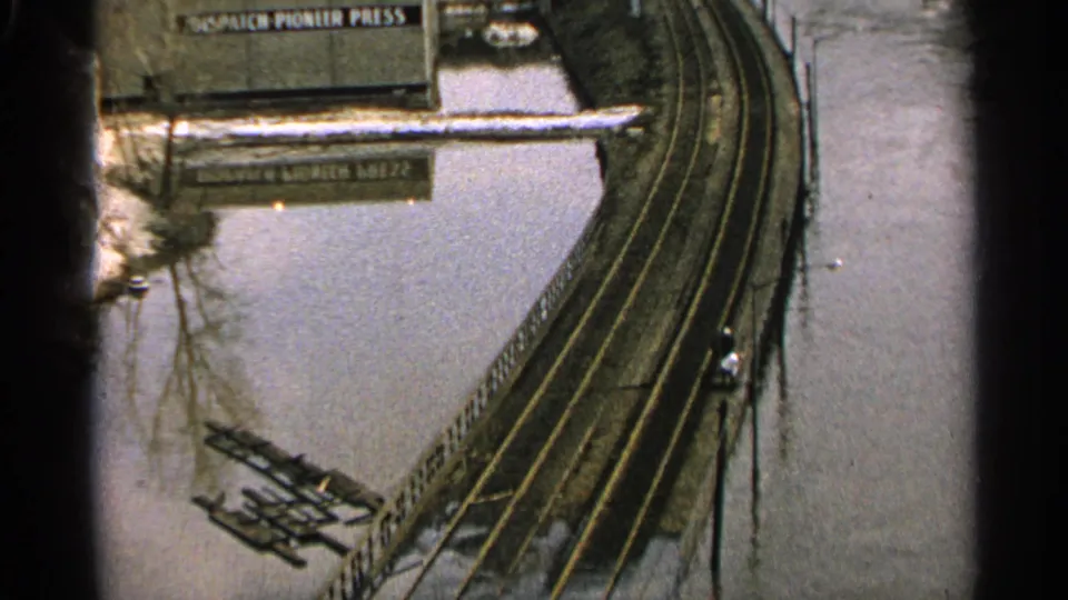 1965 Minnesota flood scene with rail tracks over high water, debris along the edge, and a readable Dispatch-Pioneer Press sign.