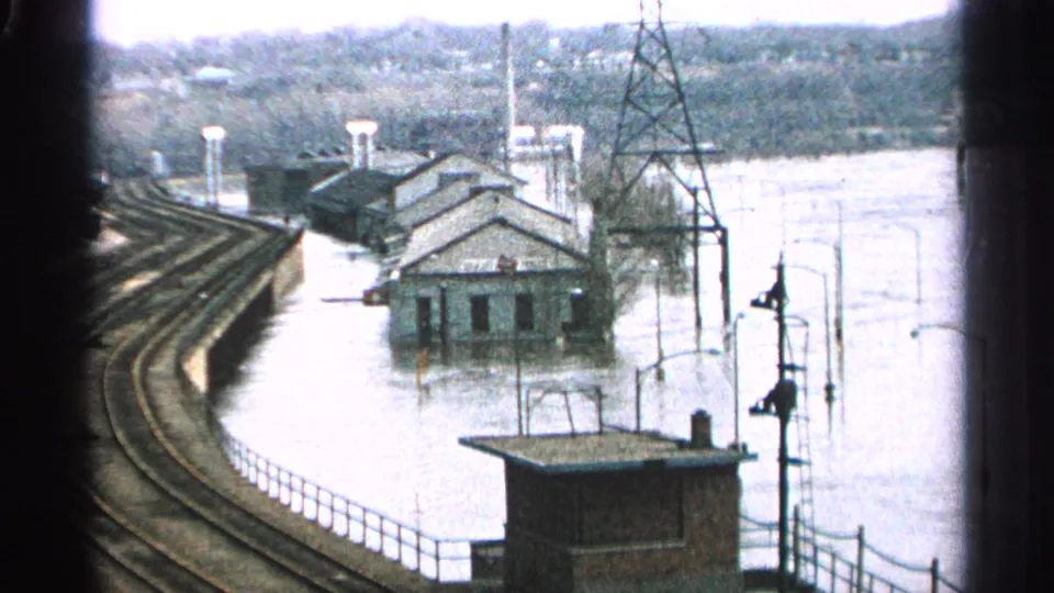 1965 Minnesota flood view showing curved rail tracks, submerged buildings, utility poles, and a small trackside structure.