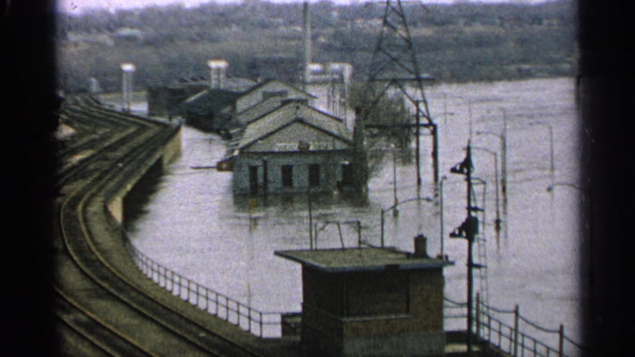 Floodwater surrounds buildings beside rail tracks in a waterside town.