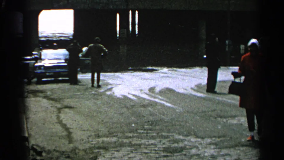1965 Minnesota flood footage showing people on a wet street near a parked car and high water beyond a dark passage.
