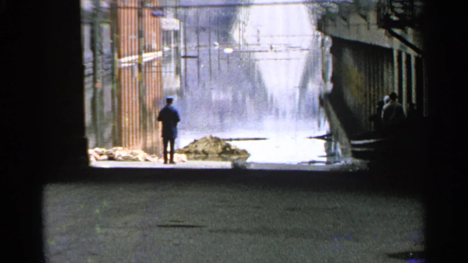 A distant person stands on wet pavement in a Minnesota dock or service area while a heavy water spray rises near buildings.