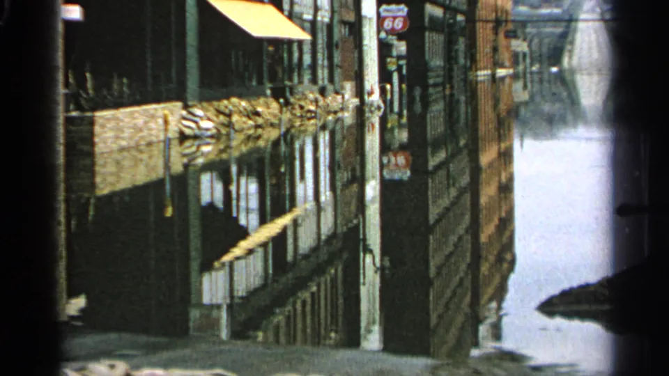 A late frame shows the flooded Minnesota street from the same angle, with storefronts, a yellow awning, utility poles, and a 66 sign visible.