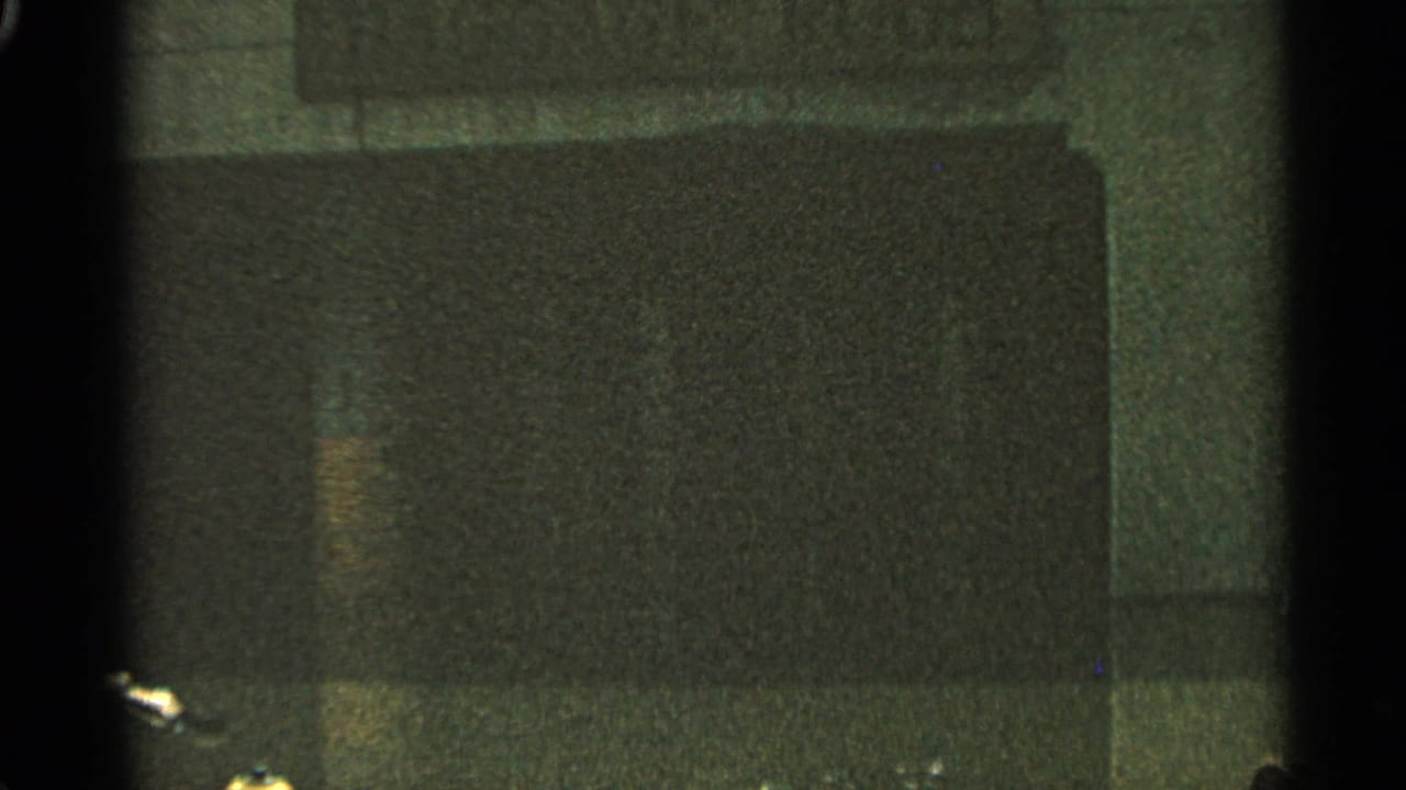 Dark, grainy frame with indistinct rectangular surface and film edge shadows.