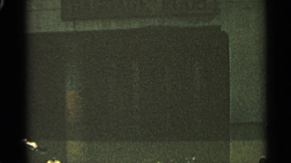 Grainy 8mm frame from the same clip, showing a dark rectangular surface with little street detail visible.