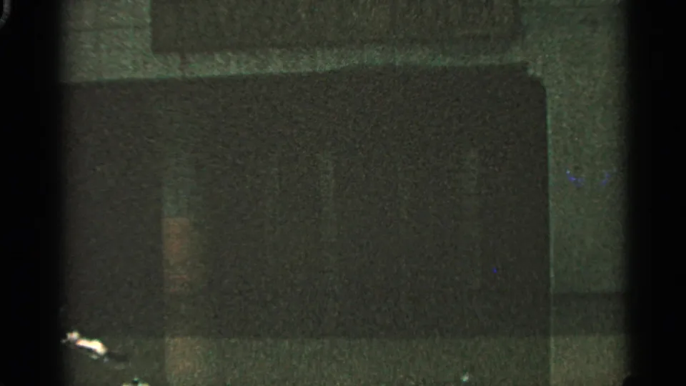 Dark 1965 8mm frame with a broad rectangular area, film grain, and faint color reflections near the lower left.