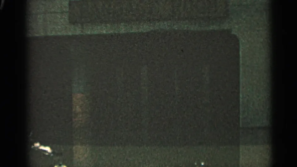 Closing 8mm frame showing a dark, indistinct surface with heavy grain and limited visible detail.