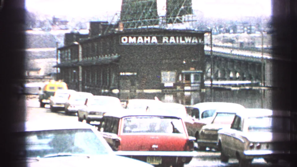 Street traffic and parked cars appear near a large Omaha Railway sign, with bright exposure and visible 1960s automobile shapes.