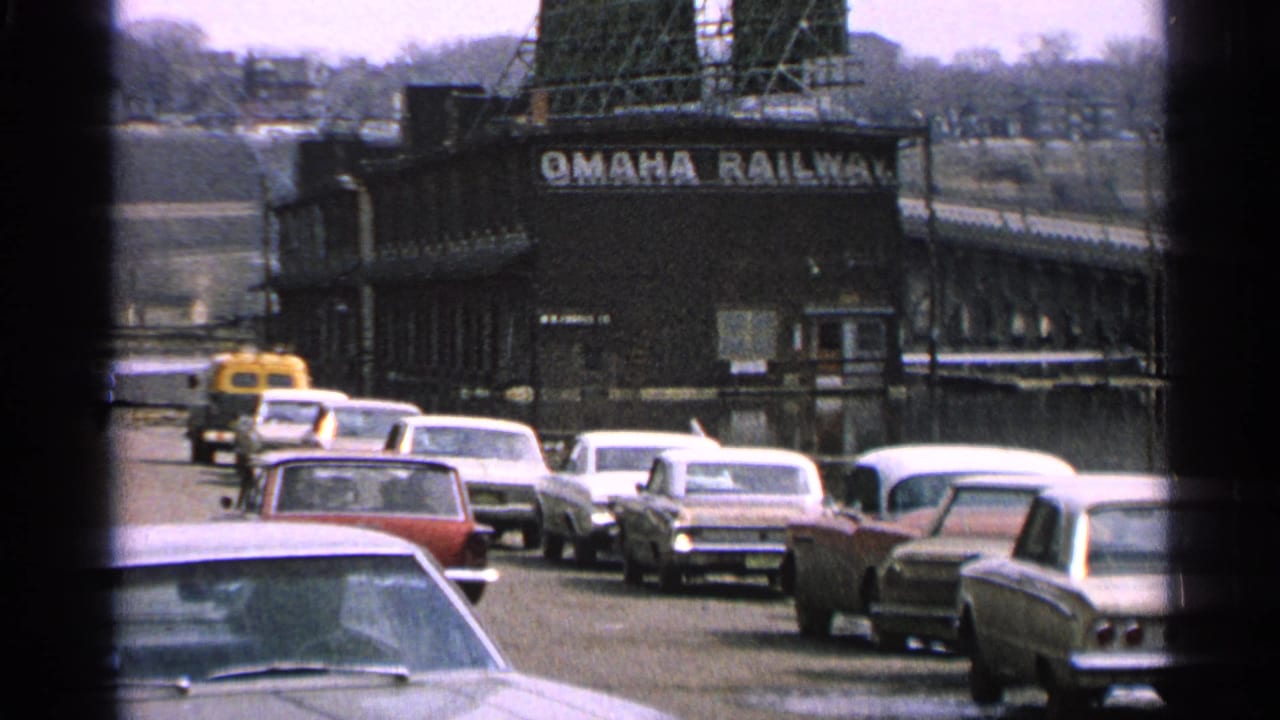Cars queue on a road beside the Omaha Railway building, seen through dark frame edges.