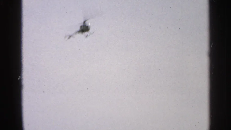 Brief 1965 Minnesota home-movie shot of a helicopter flying through a pale, grainy sky.
