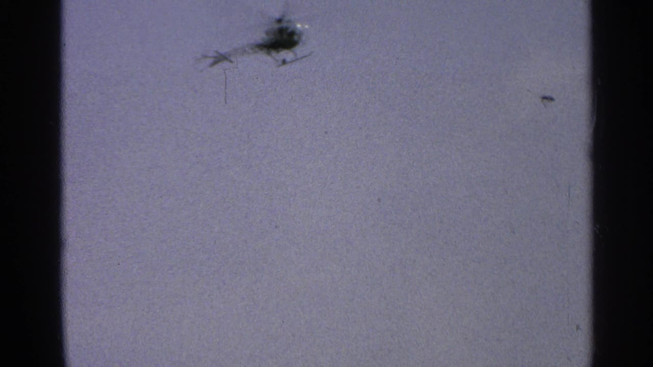 A small helicopter appears as a dark silhouette in the pale sky in 1965 Minnesota home-movie footage.