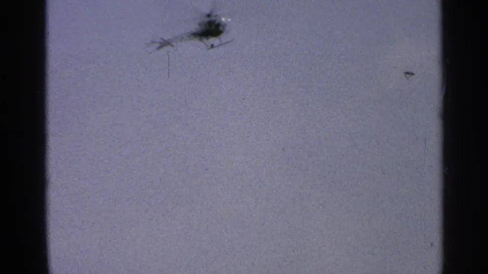 A small helicopter appears as a dark silhouette in the pale sky in 1965 Minnesota home-movie footage.