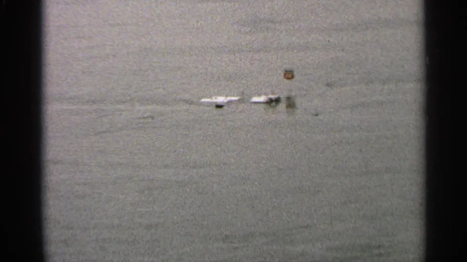 1965 Minnesota flood frame showing small boats or dock sections isolated in open water, with a small marker above the surface.