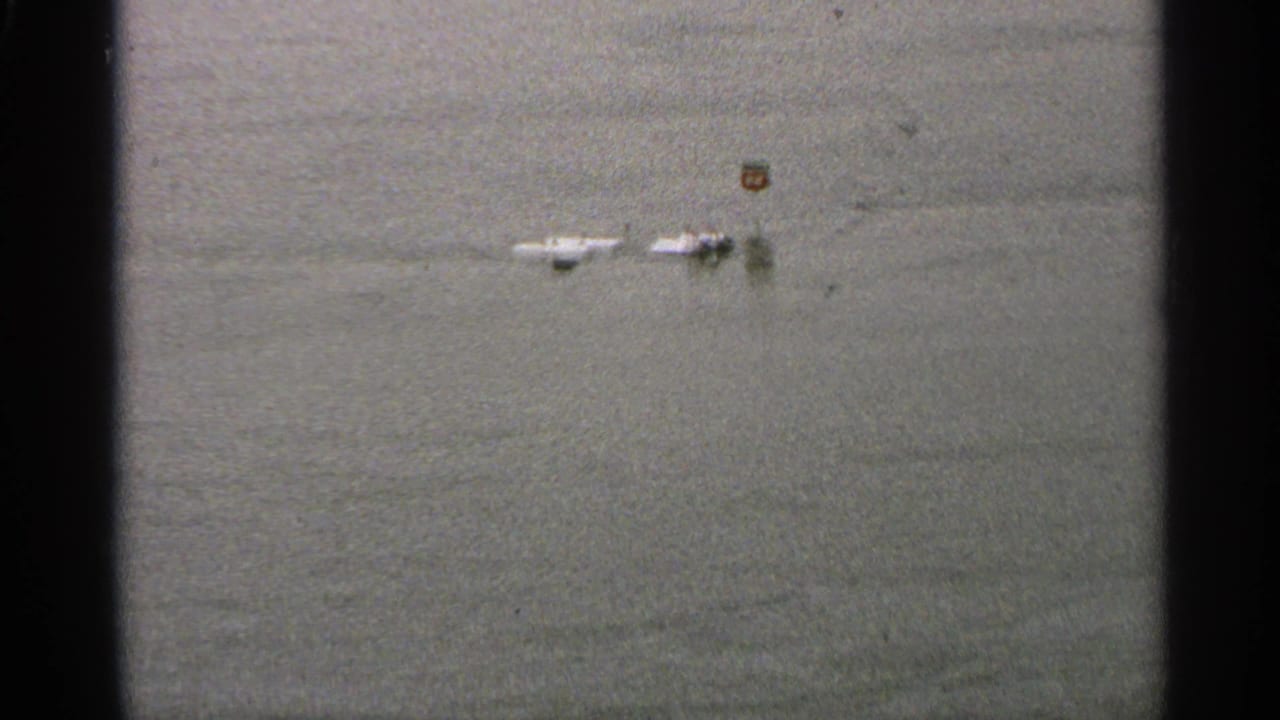 1965 Minnesota 8mm frame showing still floodwater and distant partially submerged roadside objects, with dark film edges.