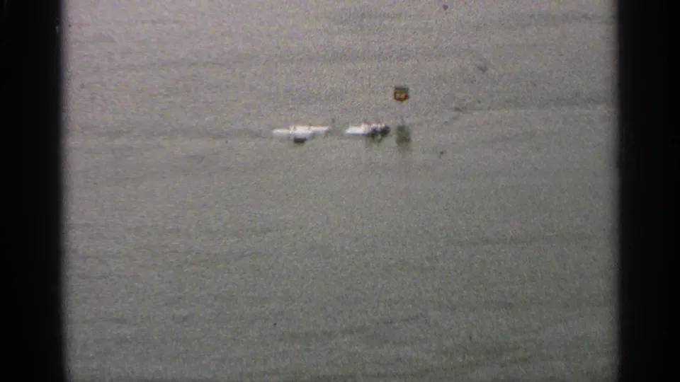 1965 Minnesota 8mm frame showing still floodwater and distant partially submerged roadside objects, with dark film edges.