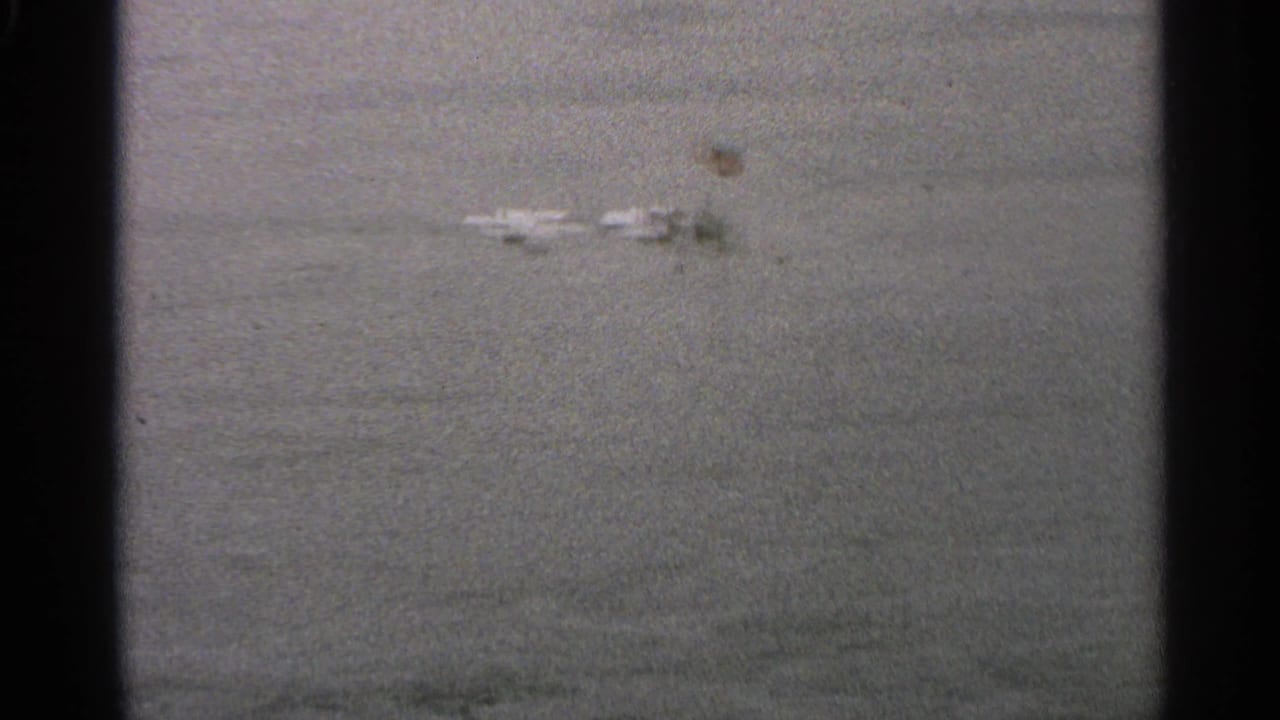 Muted 8mm view of Minnesota floodwater with a few distant roadside objects visible above the surface.