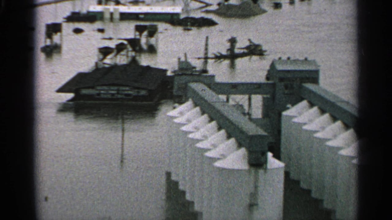 Elevated view of floodwater around an industrial building and silo rows.