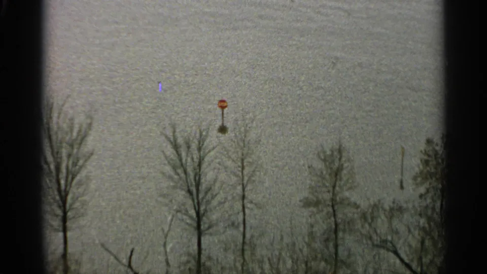 1965 Minnesota 8mm frame showing a red marker amid floodwater, with leafless trees and distant shoreline forms.