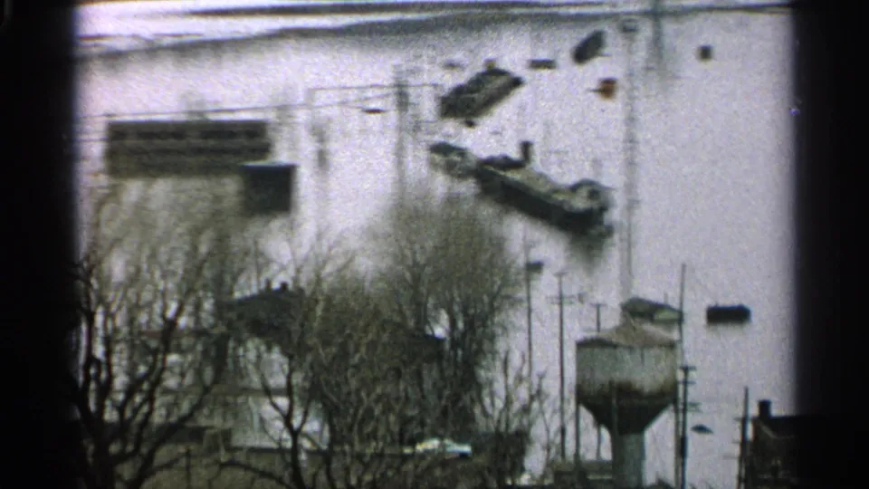 1965 Minnesota 8mm frame showing boats and debris in floodwater near docks, leafless trees, and waterfront structures.