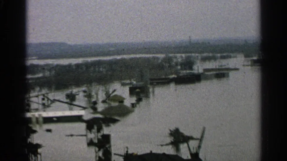 1965 Minnesota flood frame showing docks and boats near submerged shoreline structures under a hazy sky.