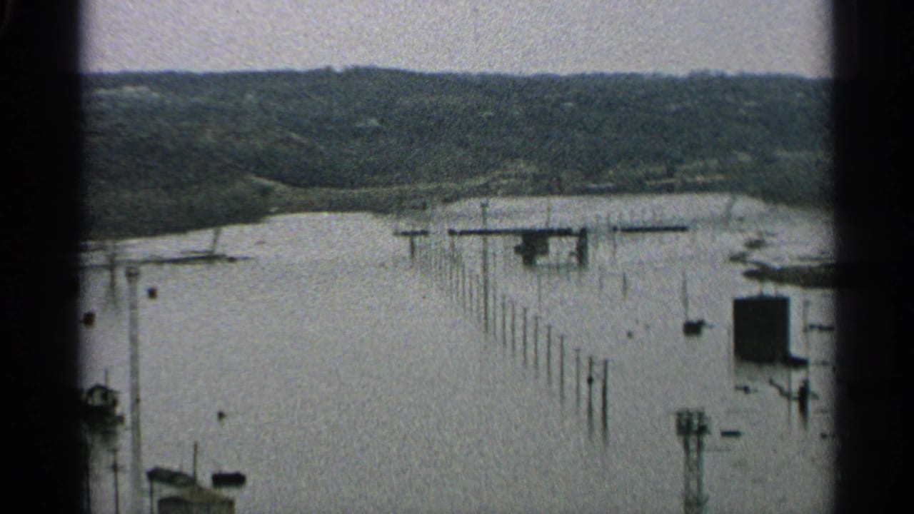 Flooded riverside with submerged dock posts and distant wooded hills.