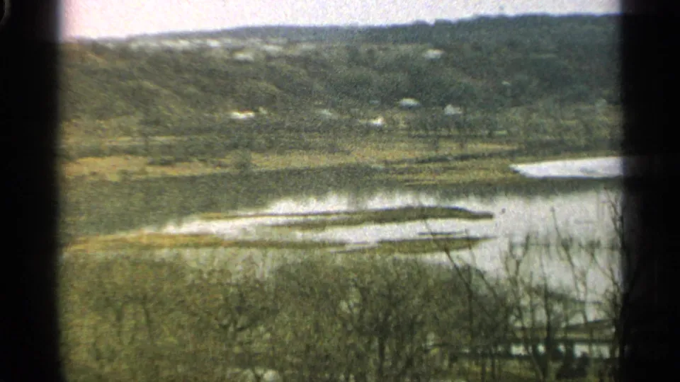 1965 Minnesota 8mm frame with floodwater spreading across a river bend, bare trees in the foreground, and low hills beyond.