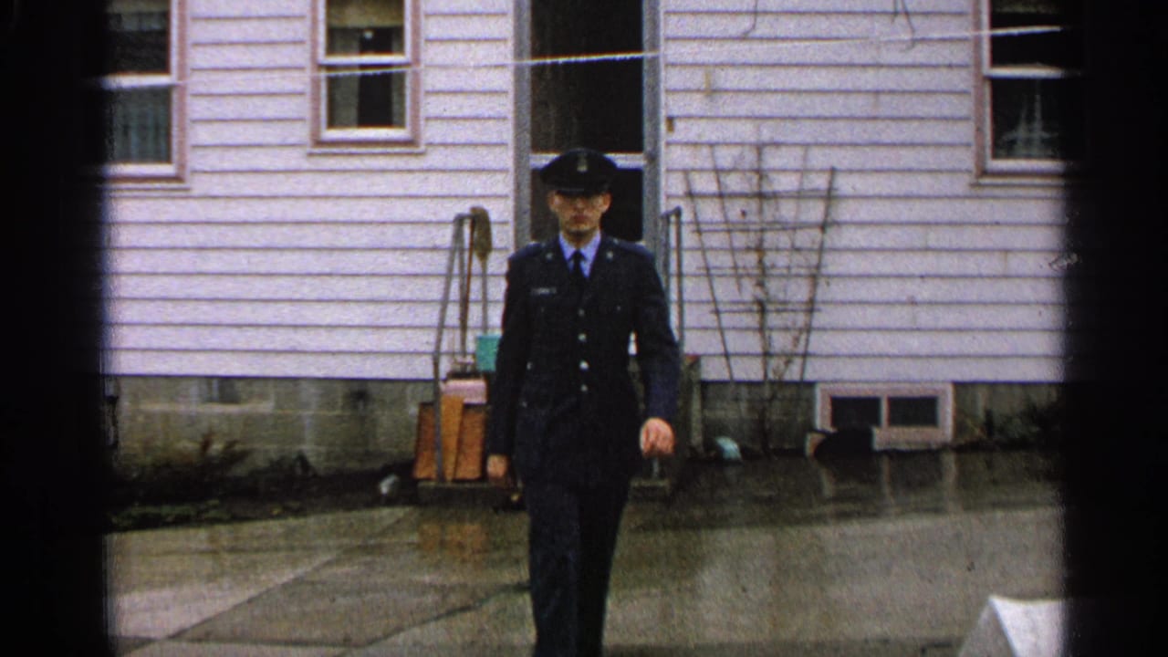 The young man in a dark blue uniform and cap continues toward the camera outside a residential house in Minnesota, 1965.