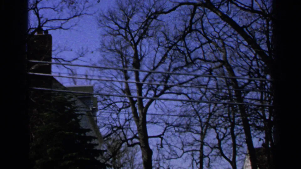 Minnesota 1965 home-movie frame showing bare trees, utility wires, and a partial house exterior under a deep blue sky.