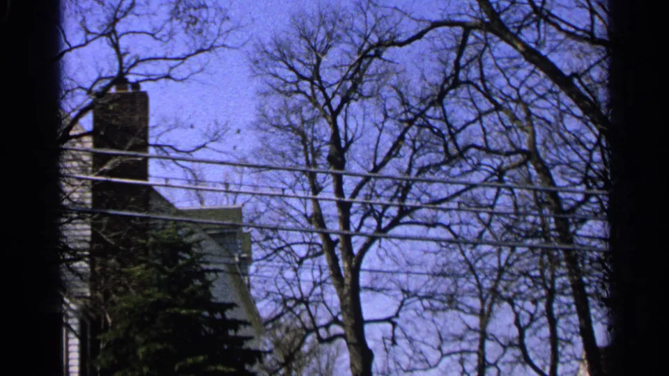 1965 Minnesota 8mm frame showing bare trees, telephone wires, and part of a chimneyed residential house.