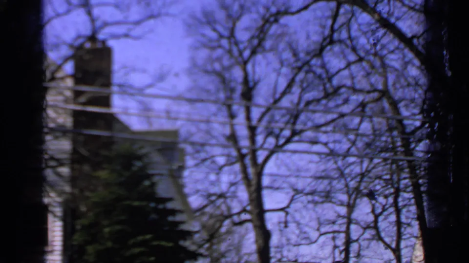 1965 Minnesota residential exterior with a chimney, leafless branches, utility wires, and soft 8mm focus.