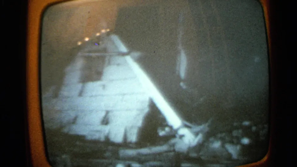 Grainy 8mm view of a rounded analog television screen with a distorted pale figure-like broadcast image.