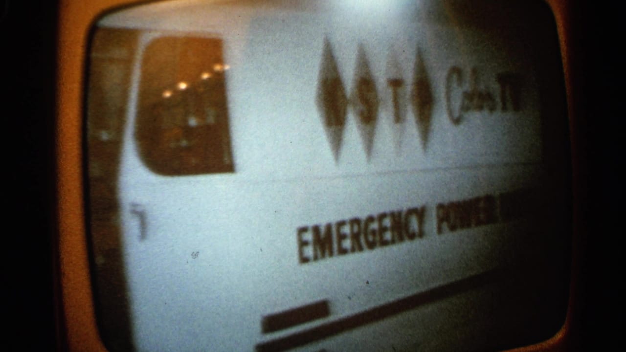 1965 Minnesota home-movie frame of a rounded television screen showing a van marked emergency power in a monochrome broadcast image.