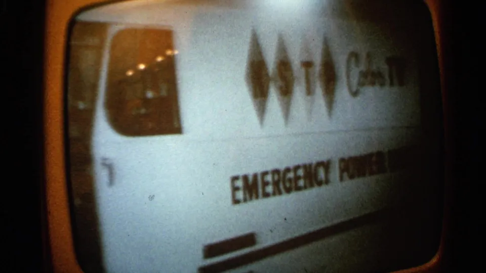 1965 Minnesota home-movie frame of a rounded television screen showing a van marked emergency power in a monochrome broadcast image.