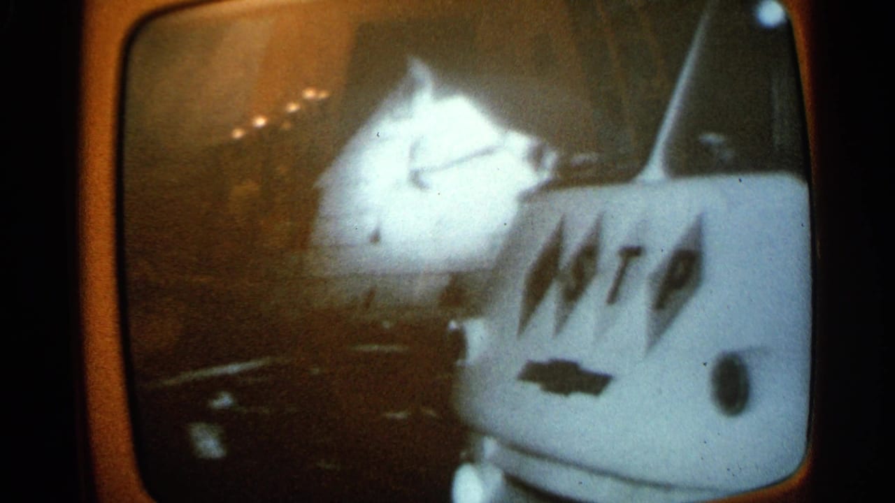 1965 Minnesota home-movie frame of a TV broadcast showing a damaged white car near a van with visible markings.