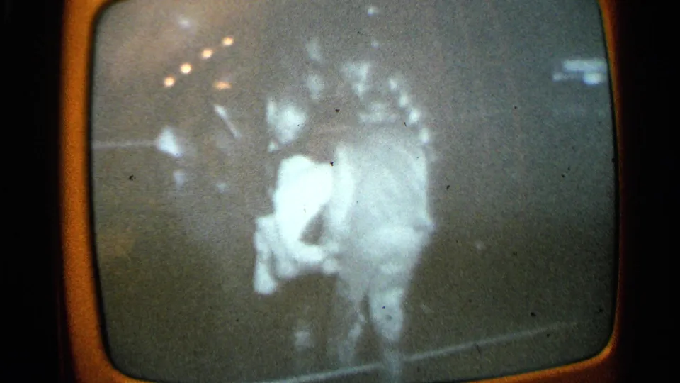 1965 Minnesota 8mm frame of a rounded TV screen with blurred monochrome footage of two indistinct figures, possibly in an emergency scene.