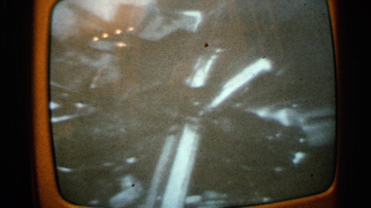Rounded TV screen in 1965 Minnesota home-movie footage showing blurred monochrome crash-like debris and strong light streaks.