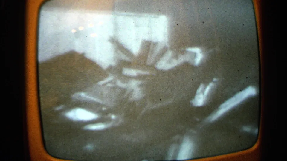 1965 Minnesota 8mm frame of a TV broadcast where an indistinct figure appears near a possible stretcher or carried object.