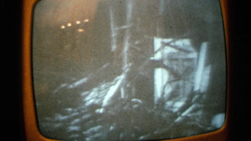 Rounded TV screen in 1965 Minnesota home-movie footage showing a distorted black-and-white crash scene with debris and vertical forms.