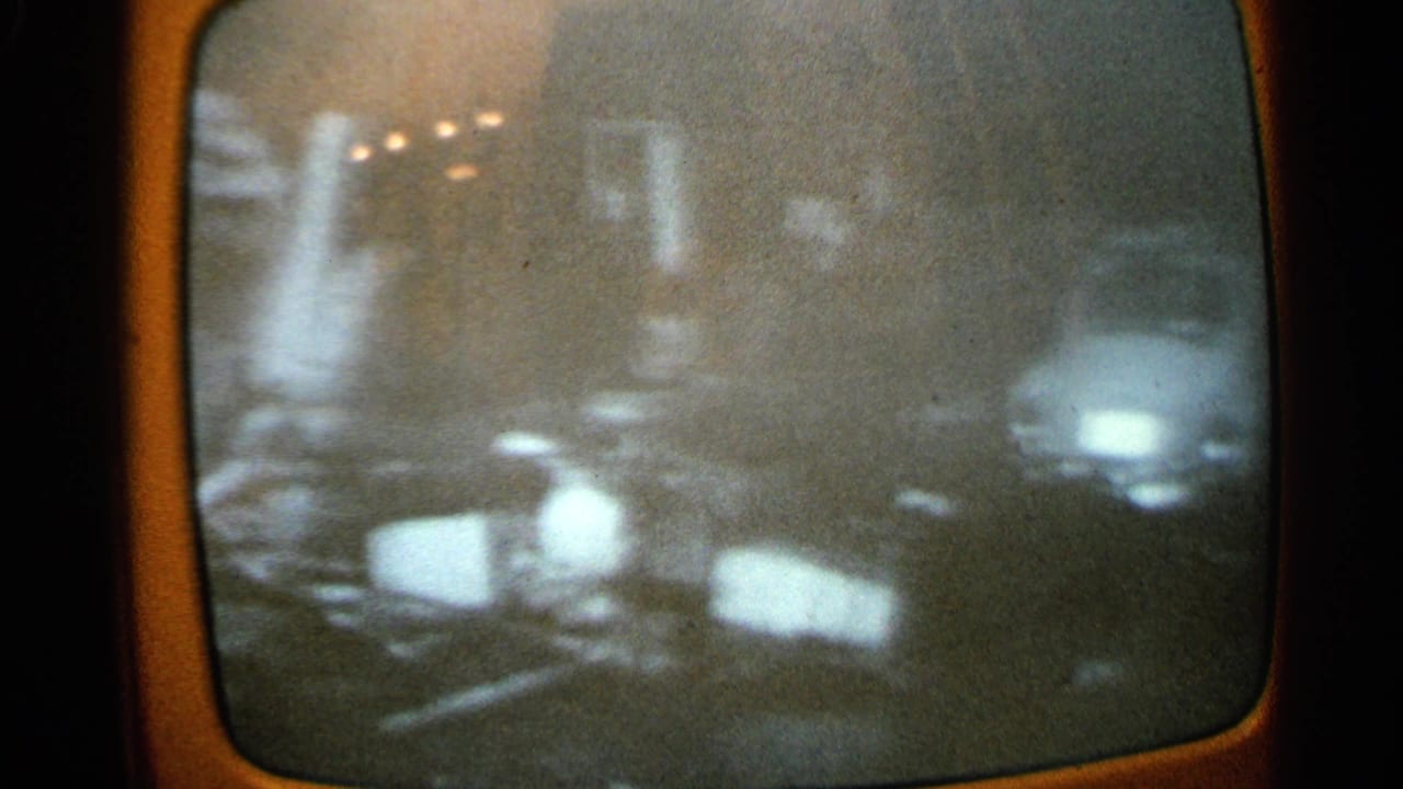 1965 Minnesota 8mm frame of a television screen with indistinct rubble or ground debris, bright highlights, and heavy film grain.