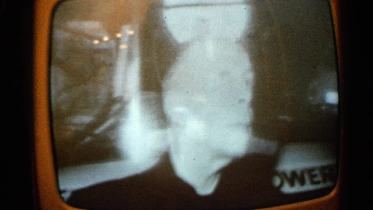 Television screen showing a pale close view with partial lettering near the lower right edge.