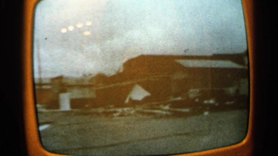1965 Minnesota 8mm frame showing a low rural building, snow-covered ground, and scattered material in a soft, grainy screen recording.