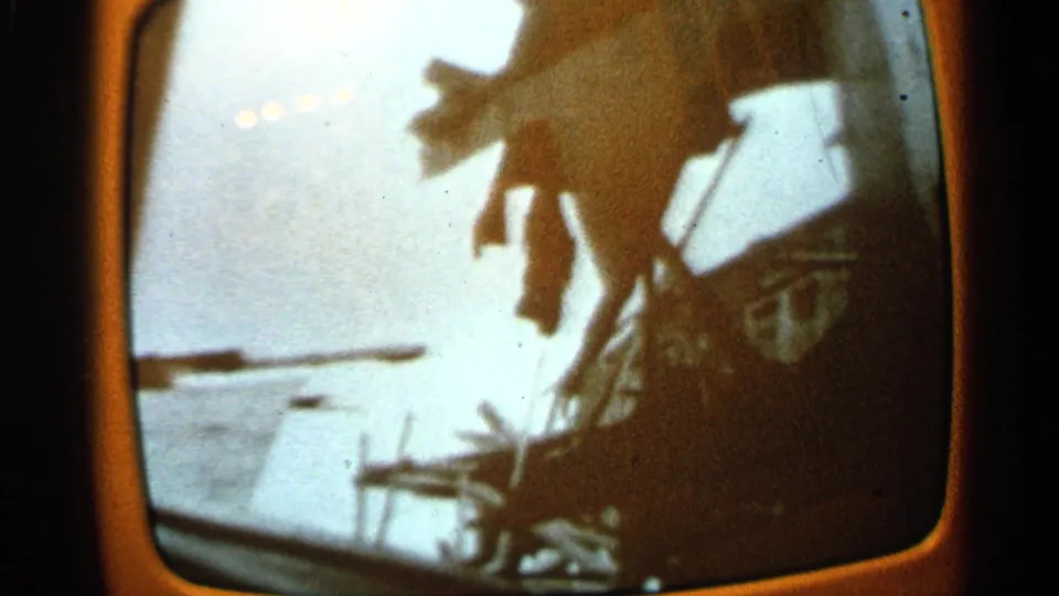 1965 Minnesota 8mm frame with a dark damaged structure, dangling debris, snow beyond it, and strong exposure contrast inside the screen border.