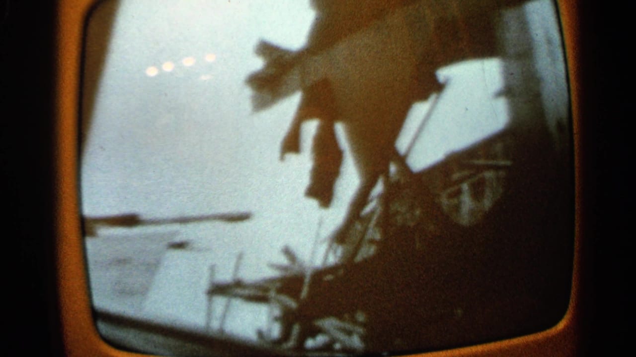 1965 Minnesota 8mm frame of a curved TV screen with a dim view of broken roof lines and shadowed debris.