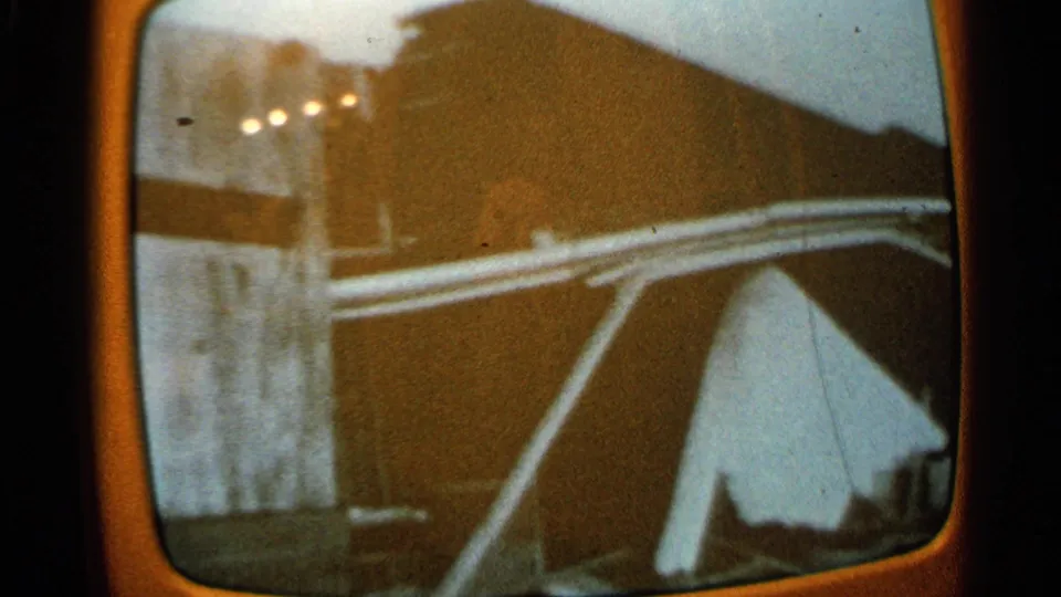 1965 Minnesota home-movie frame with a TV-screen view of slanted roof material, pale beams, and a deteriorated interior surface.