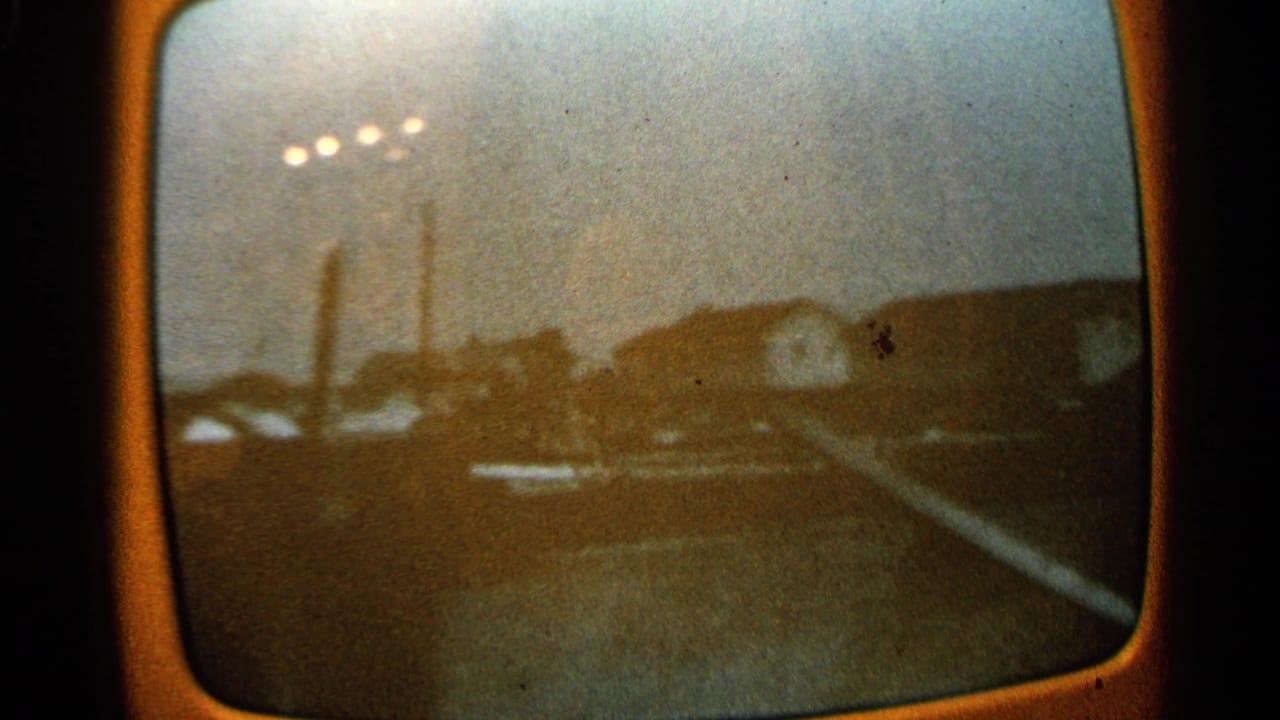 Soft view of an industrial area seen through a rounded screen, with streetlights, stacks, buildings, and debris.