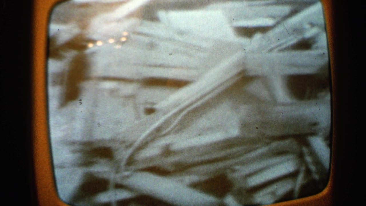 1965 Minnesota home-movie frame showing scattered wreckage and broken building materials inside a rounded screen-like image area.