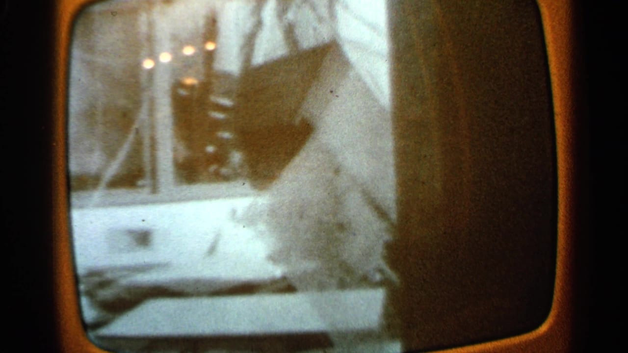 1965 Minnesota frame showing part of a damaged residence or structure with debris and visible screen reflections.
