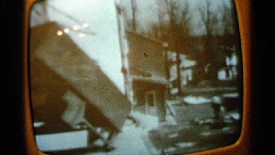 1965 Minnesota home-movie frame showing damaged building material near a house and bare trees under pale outdoor light.