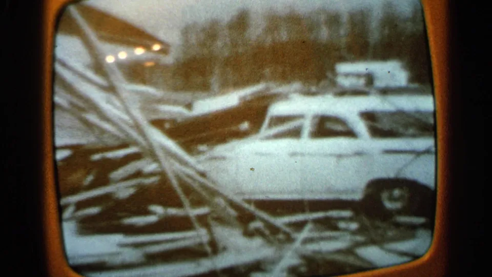 1965 Minnesota frame showing a light-colored car near collapsed boards and scattered disaster debris.