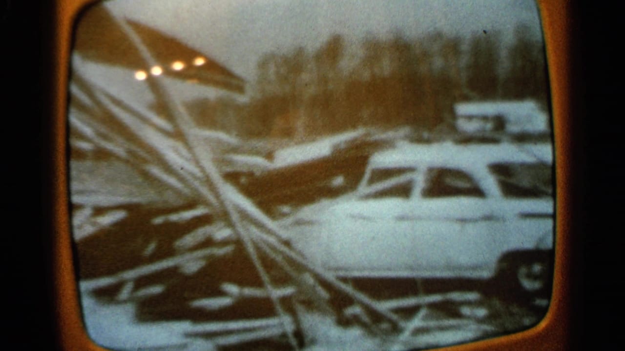 1965 Minnesota home-movie frame of a vintage television displaying a white car near fallen branches and winter debris.